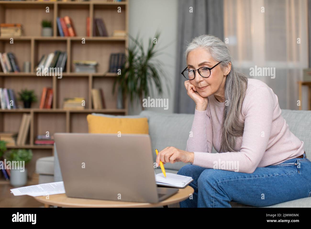 Sérieuse fatiguée occupée caucasien senior gris-cheveux femme enseignant dans des lunettes travail au portable dans le salon intérieur Banque D'Images