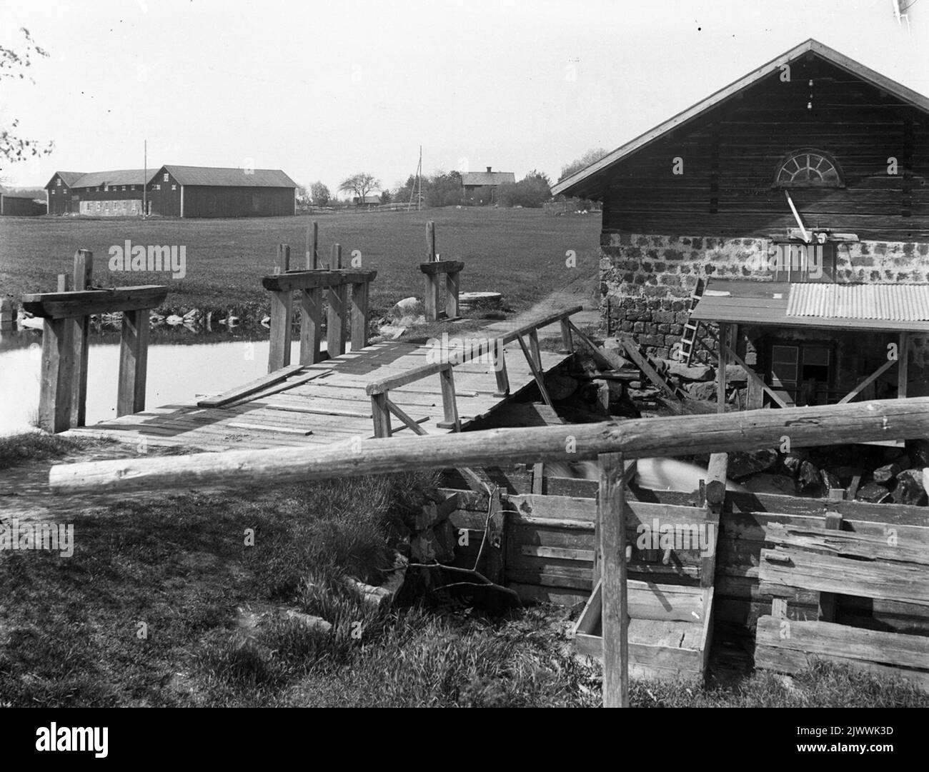 Le moulin avec Åsmundshyttan n° 6 champs et dépendances de Mattsas en arrière-plan. La boîte carrée devant la gouttière a été utilisée pour laver les pommes de terre lorsque les villageois feraient de la farine de pommes de terre. Au premier plan, la gouttière descend jusqu'à la roue d'eau sur le journal de battage. Kvarnen med Åsmundshyttan nr 6 'Mattsas' åkrar och uthus i bakgrunden. Den fyrkantiga lådan framför rännan användes att tvätta potatis i när byborna skulle göra potatismjöl. Je förgrunden rännan ner till vattenhjulet på trösklogen. Banque D'Images