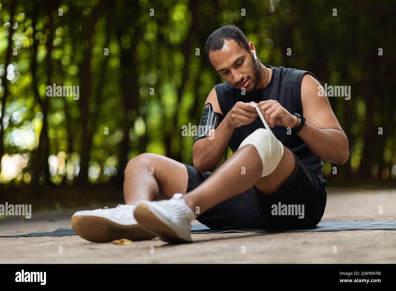 Sportif afro-américain enveloppant le genou blessé avec un bandage élastique Banque D'Images
