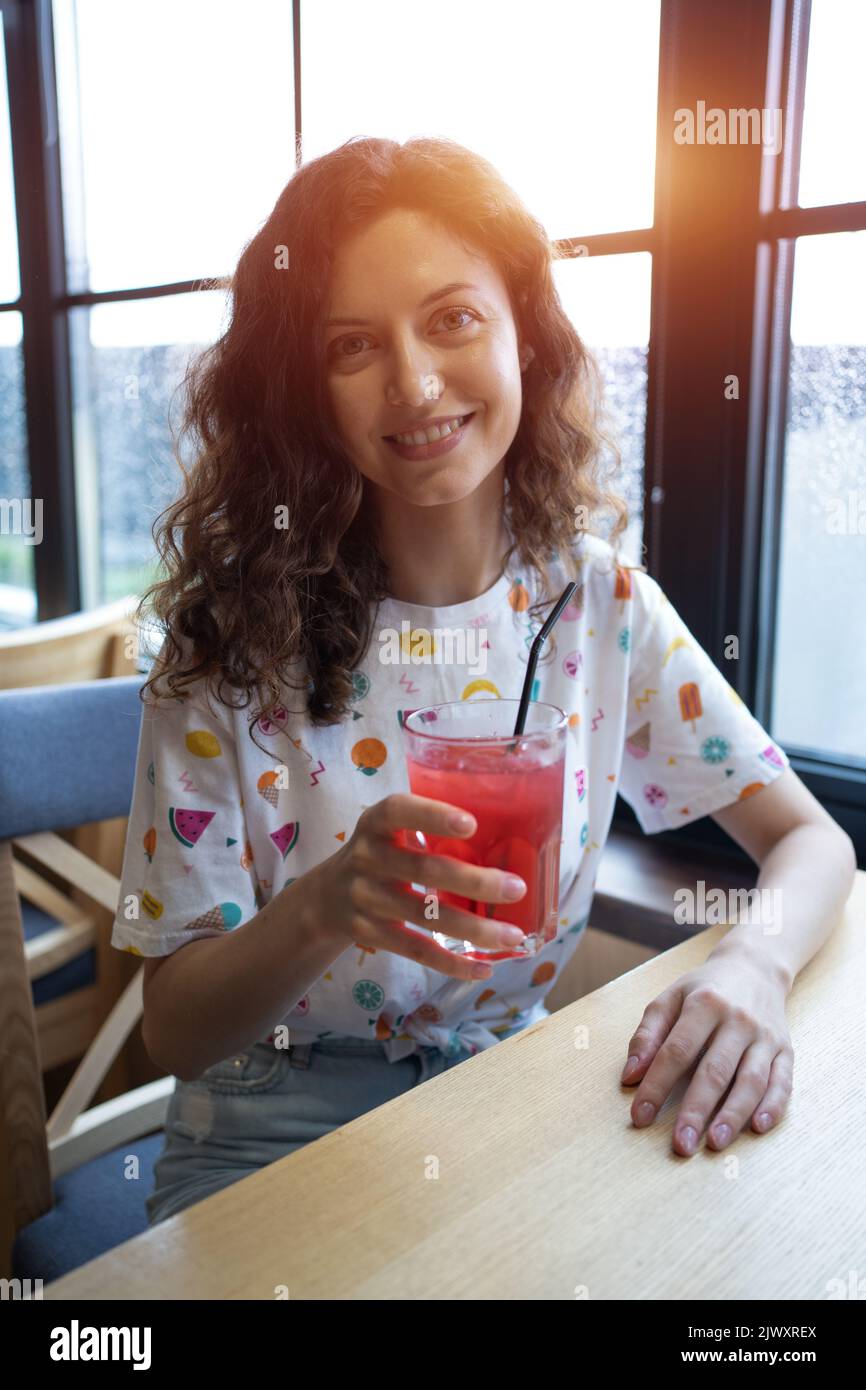 souriant et joyeux, une femme boit du jus de fruits aux baies avec du soda au café Banque D'Images