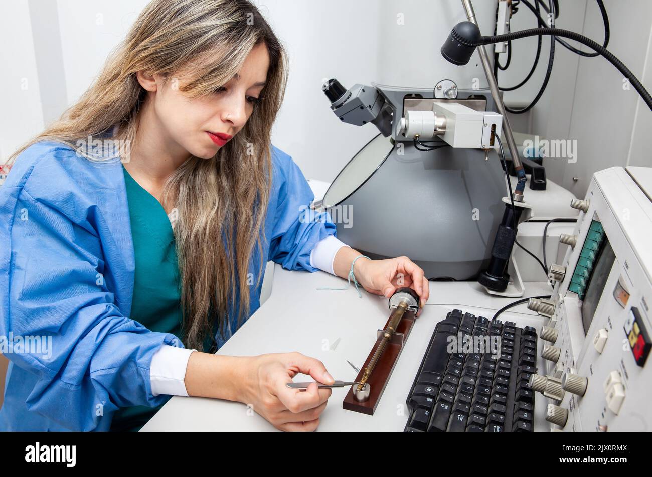 Une jeune scientifique femelle charge une grille avec un échantillon sur le porte-échantillon d'un microscope électronique à transmission Banque D'Images