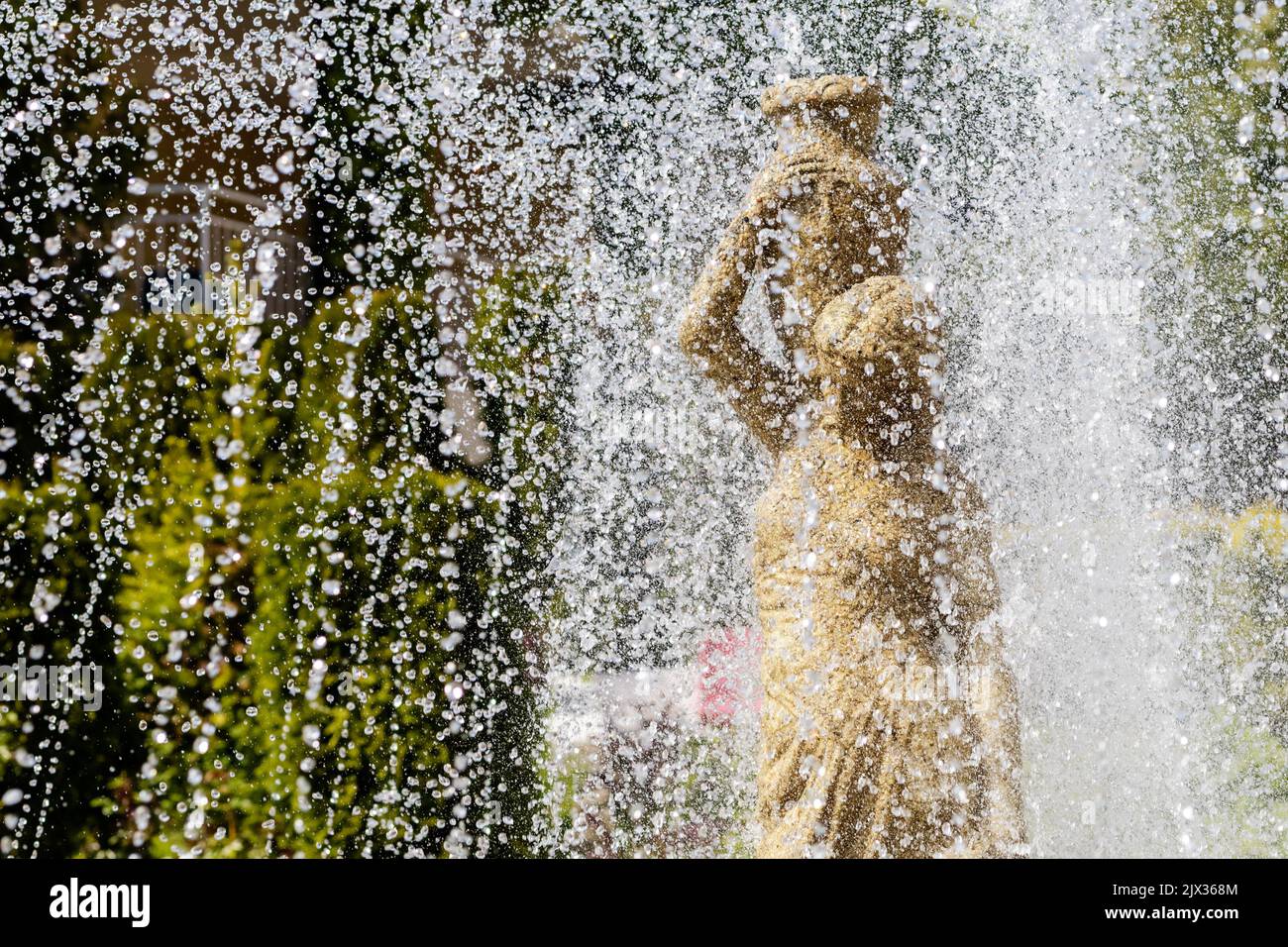 Une fontaine en gros plan coule au-dessus d'une statue de femme. Éclaboussures d'eau et sculpture en pierre d'une fille avec verseuse Banque D'Images
