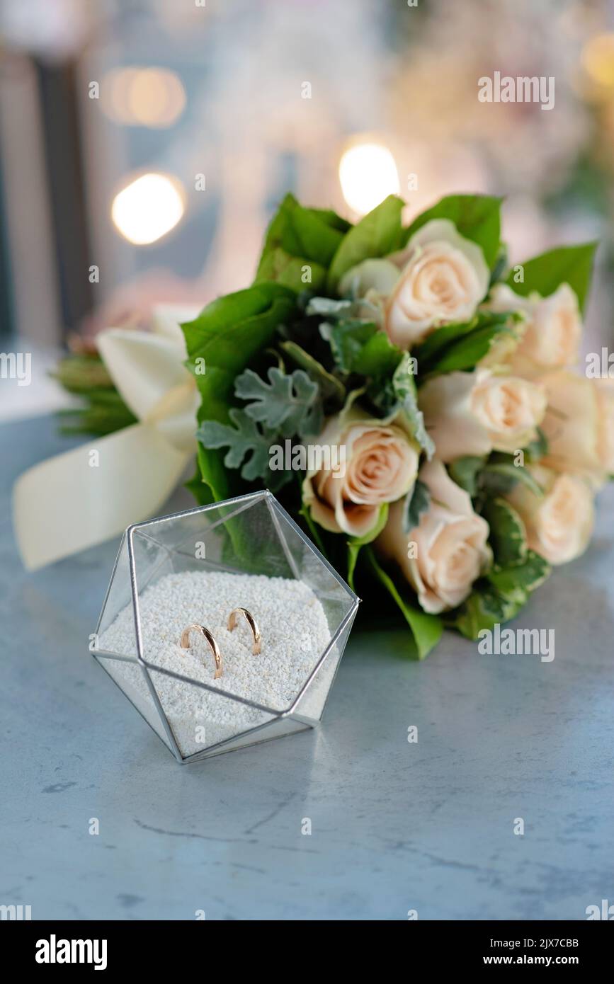 Une paire de magnifiques anneaux de mariage dans un support en verre moderne et un délicat bouquet de roses de mariée. Mariage, cérémonie. Mise au point sélective douce. Banque D'Images Une paire de magnifiques anneaux de mariage dans un support en verre moderne et un délicat bouquet de roses de mariée. Mariage, cérémonie. Mise au point sélective douce. Banque D'Images