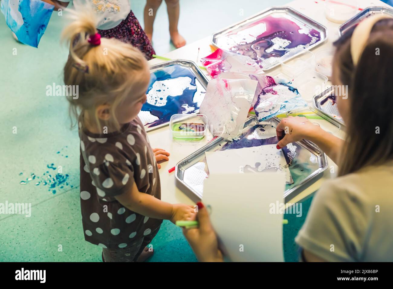 Petite fille cute caucasienne avec d'autres enfants peinture au lait, ajoutant la coloration de la nourriture au lait avec un enseignant dans la salle de classe à l'école maternelle. Photo de haute qualité Banque D'Images