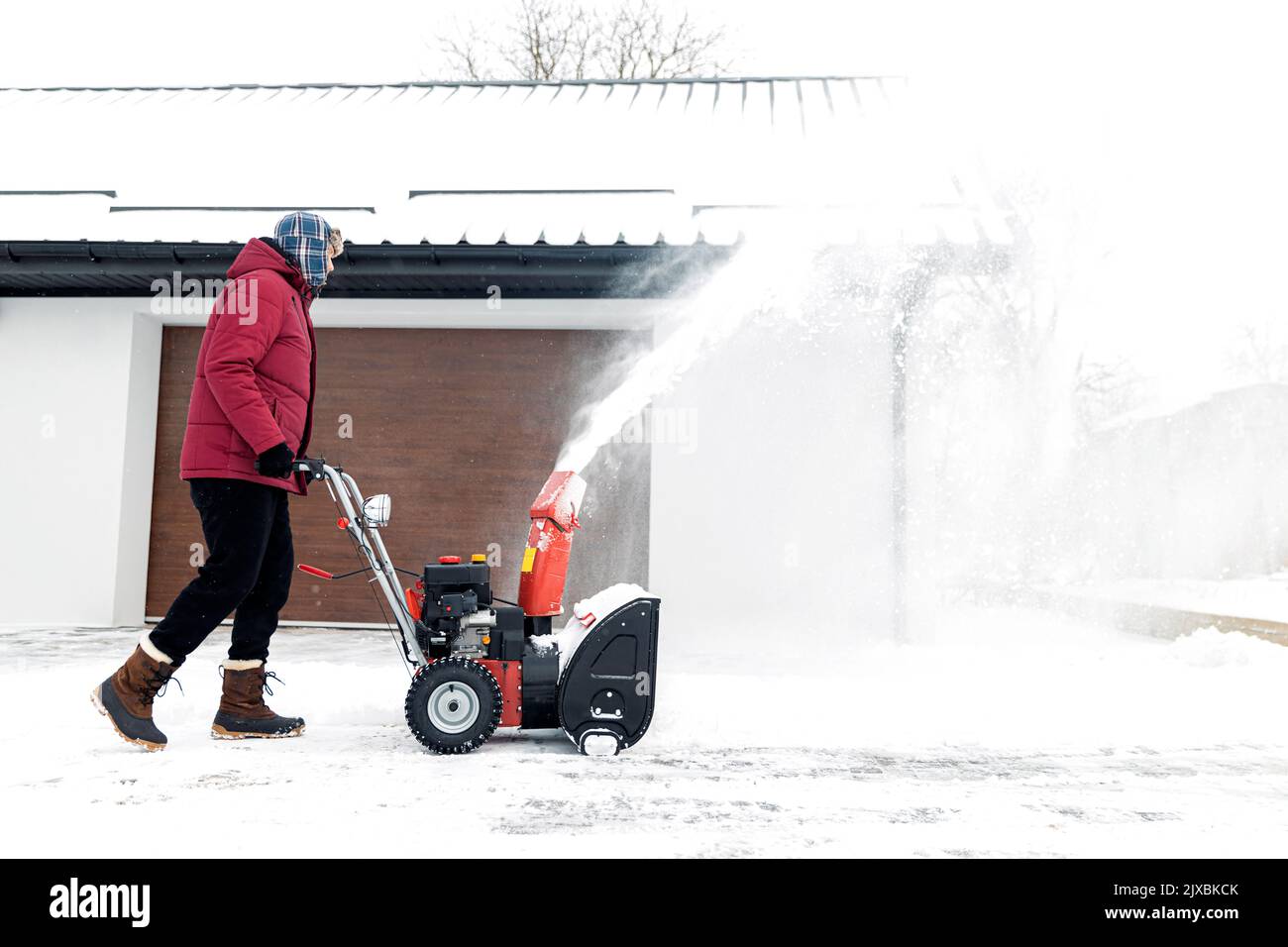 Souffleuse à neige alimentée par l'essence en action. Homme à l'extérieur devant la maison utilisant une souffleuse à neige. Déneigement, assistant de fraise en hiver à l'extérieur de la maison. Un jeune travailleur qui soufflait de neige pendant un blizzard Banque D'Images