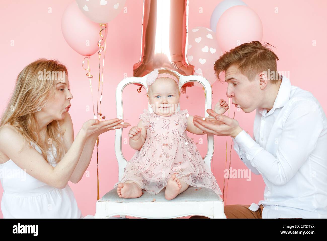 Petit peu souriant, heureux pieds nus un enfant d'un an en robe rose assis sur une chaise lors d'une fête d'anniversaire Banque D'Images