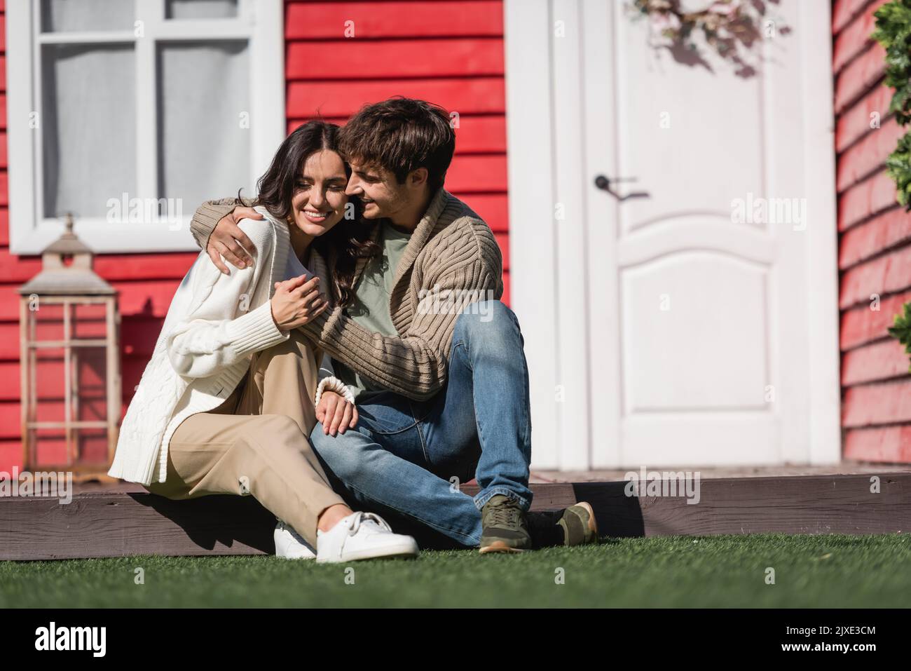 Jeune couple gai dans cardigans embrassant sur la terrasse de la maison, image de stock Banque D'Images