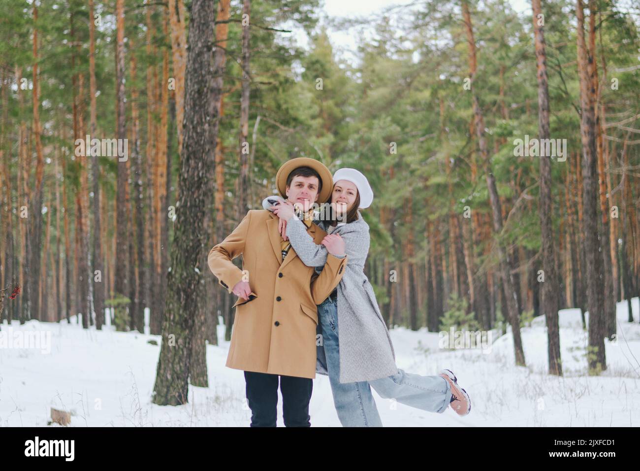 drôle de famille, couple dans le parc enneigé, forêt. Une jeune femme, une fille et un homme en chapeau marchant près de pins enneigés. Boire du café. Amuse-toi bien. Famille Banque D'Images