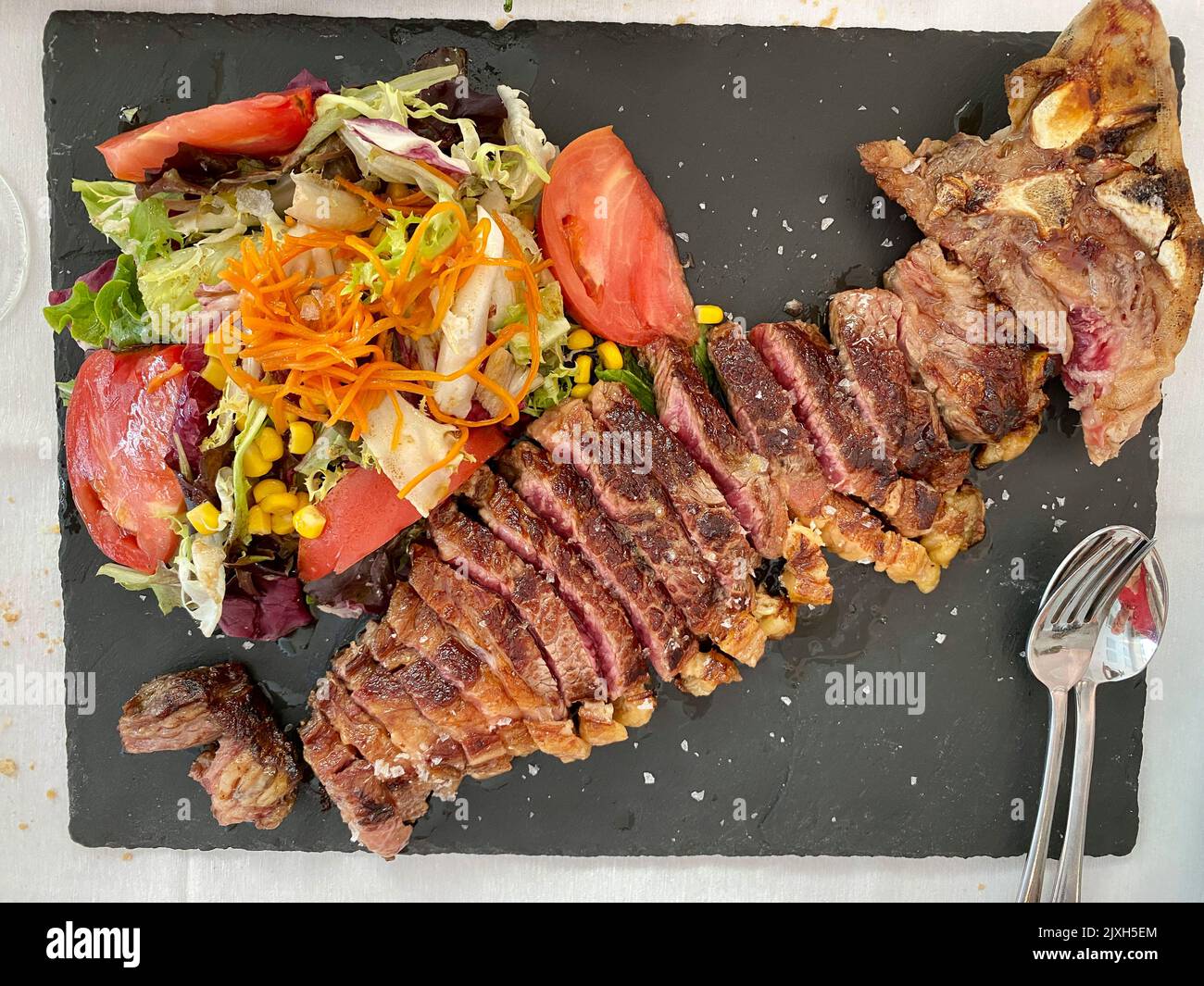 Steak de veau cuit avec salade et légumes. Sur fond noir. Vue de dessus. Style rustique. Banque D'Images