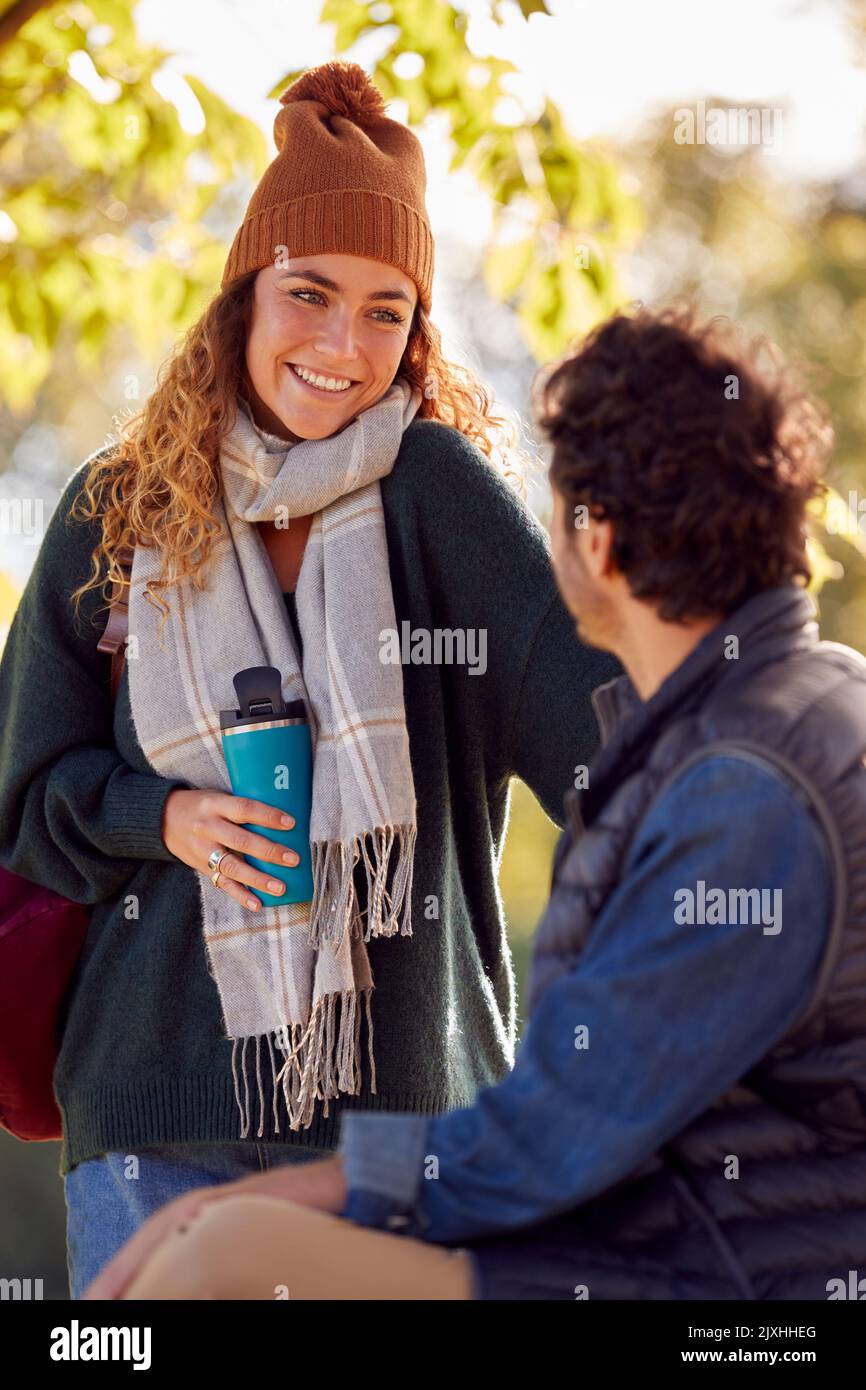 Couple souriant avec un homme assis sur le banc dans le parc d'automne saluant l'un l'autre Banque D'Images
