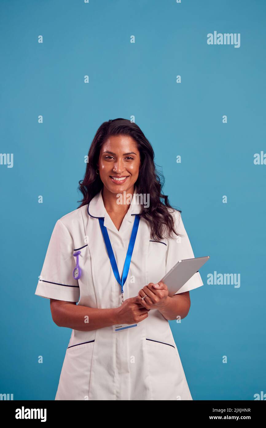 Femme souriante mature infirmière portant un uniforme avec une tablette numérique devant un arrière-plan de studio bleu Banque D'Images