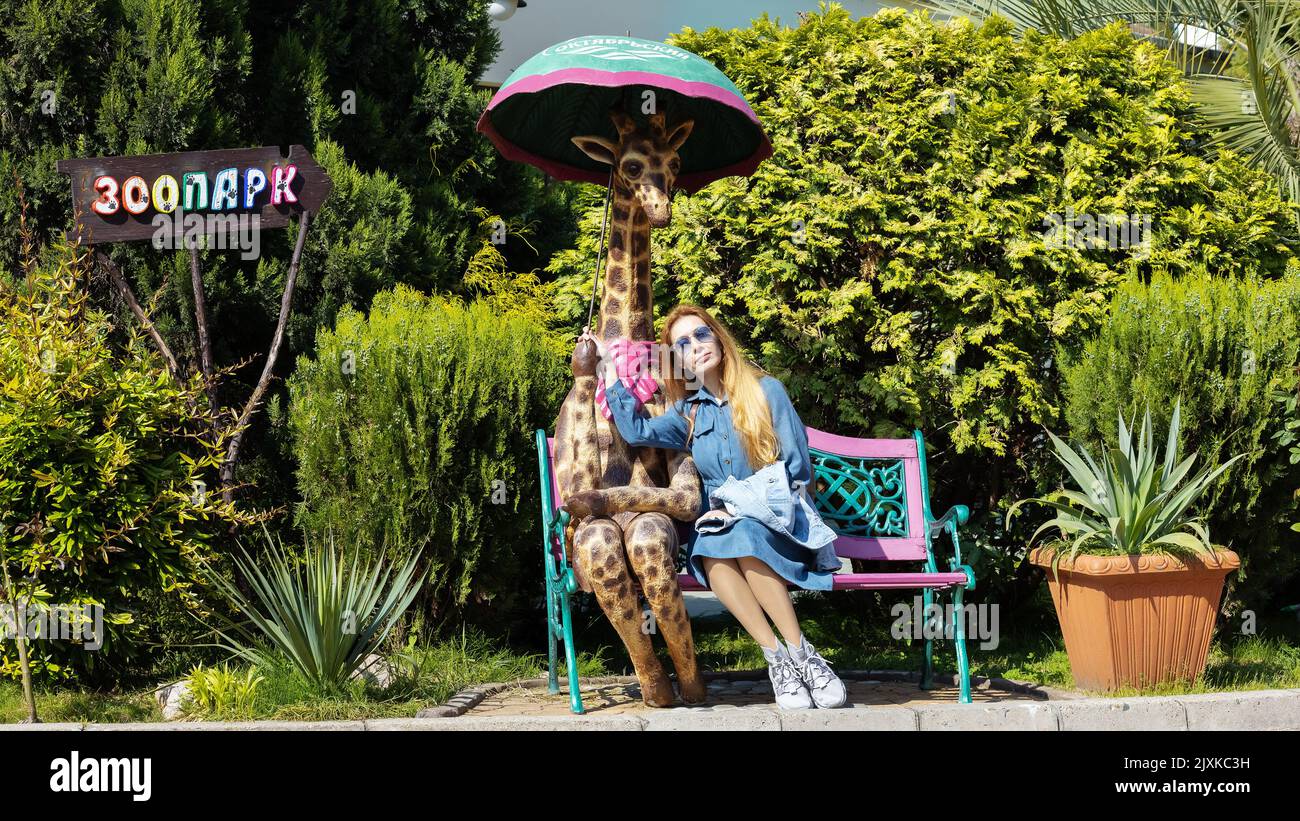 Russie, Sotchi 15.05.2022. La fille est assise sur le banc avec une figurine d'une girafe. À gauche se trouve une flèche qui indique Zoo Banque D'Images