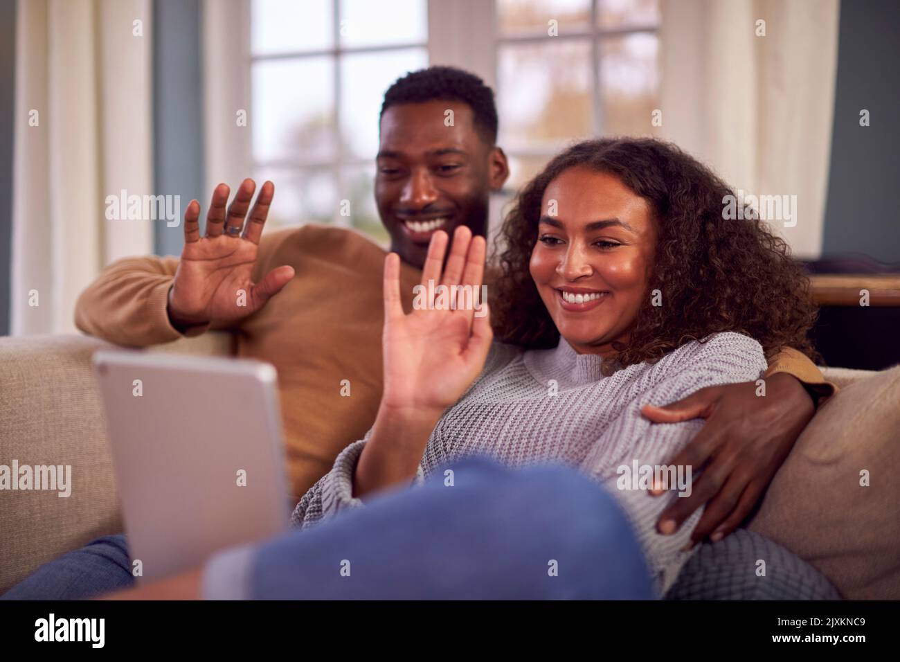 Couple souriant assis sur un canapé à la maison passer un appel vidéo sur une tablette numérique Banque D'Images