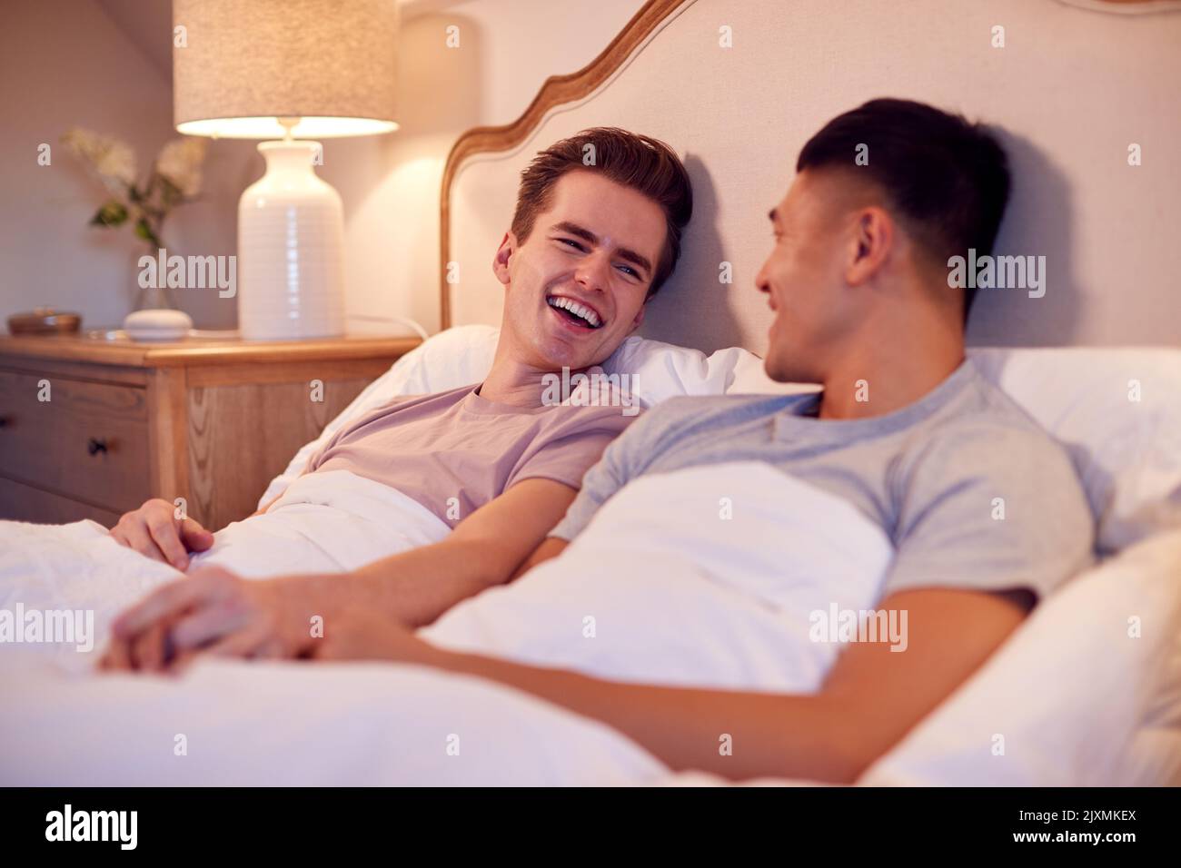 Aimer le même sexe masculin couple allongé dans le lit à la maison tenant les mains ensemble Banque D'Images