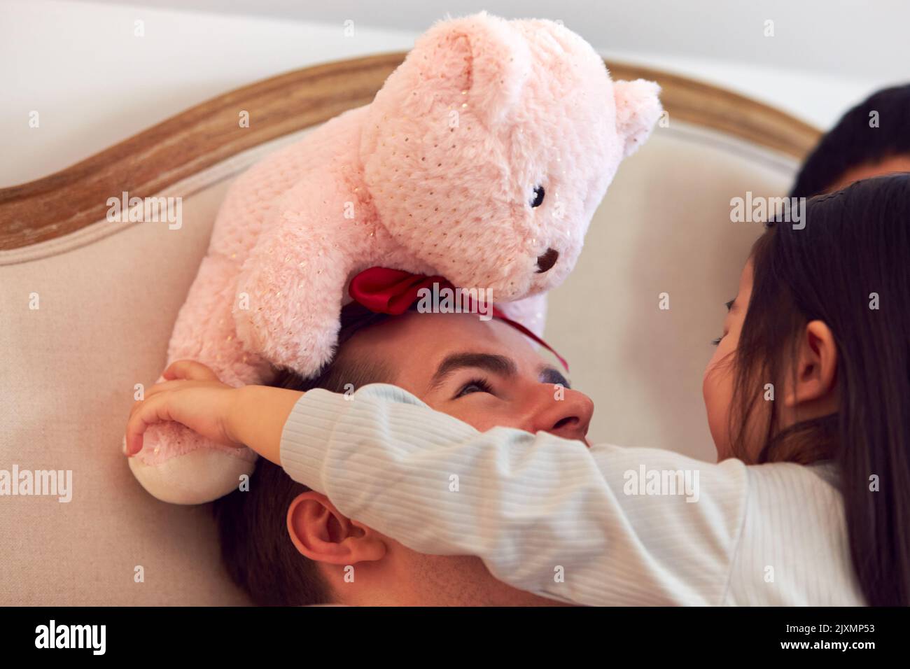 Famille avec papa au lit à la maison jouant au jeu avec sa fille et son jouet doux Banque D'Images