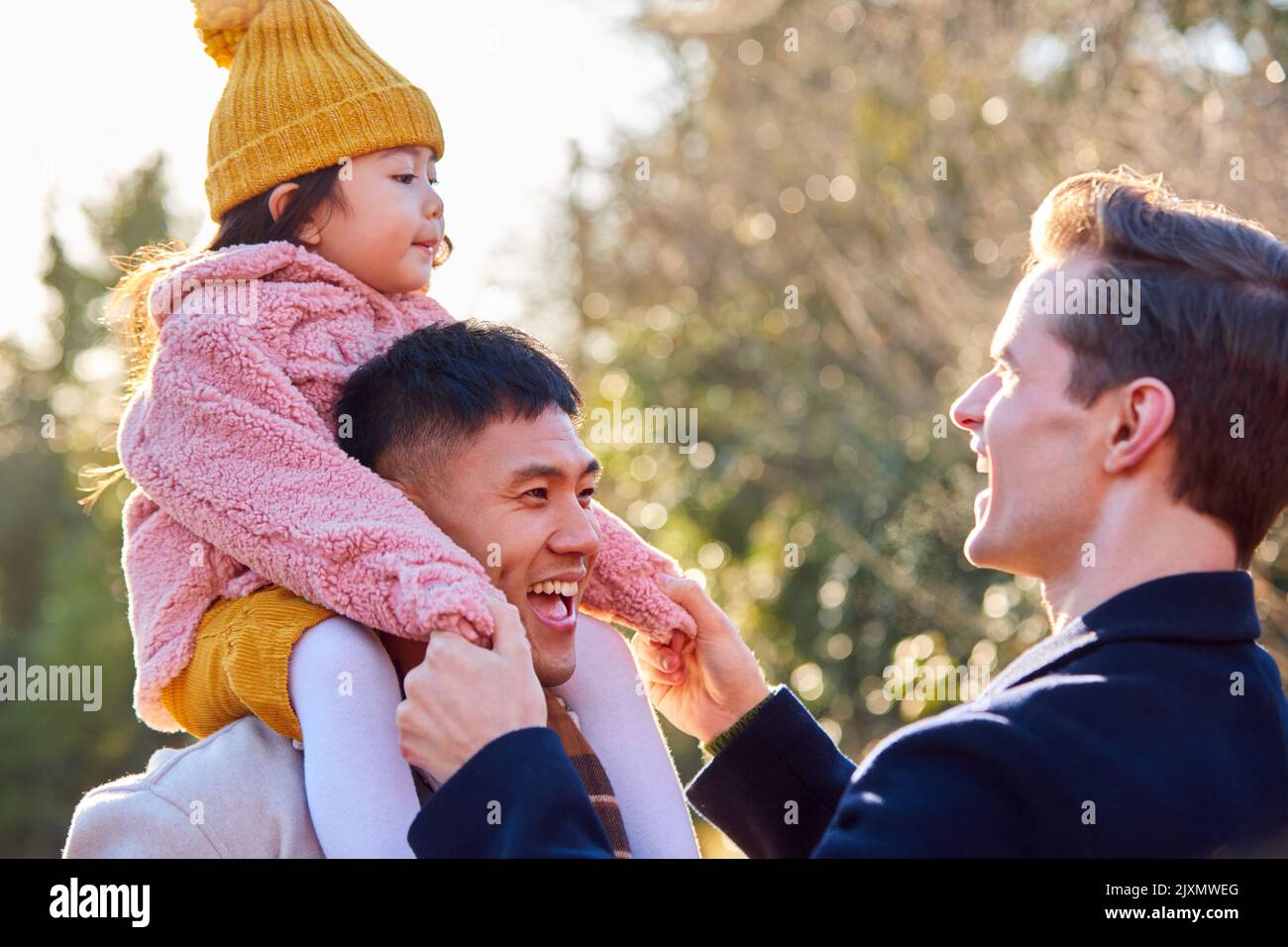 Famille avec deux Dads sur la marche dans la campagne d'hiver portant la fille sur les épaules Banque D'Images