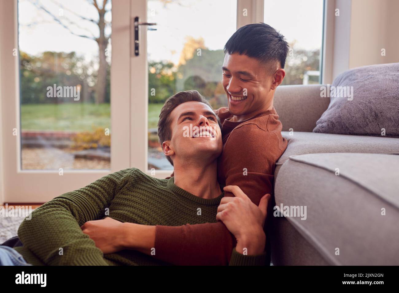 Aimer le même sexe masculin couple cuddling sur canapé à la maison ensemble Banque D'Images
