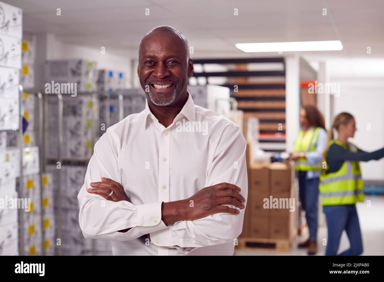 Portrait du chef d'équipe masculin de l'entrepôt avec le personnel en charge de la cueillette des articles sur les tablettes en arrière-plan Banque D'Images