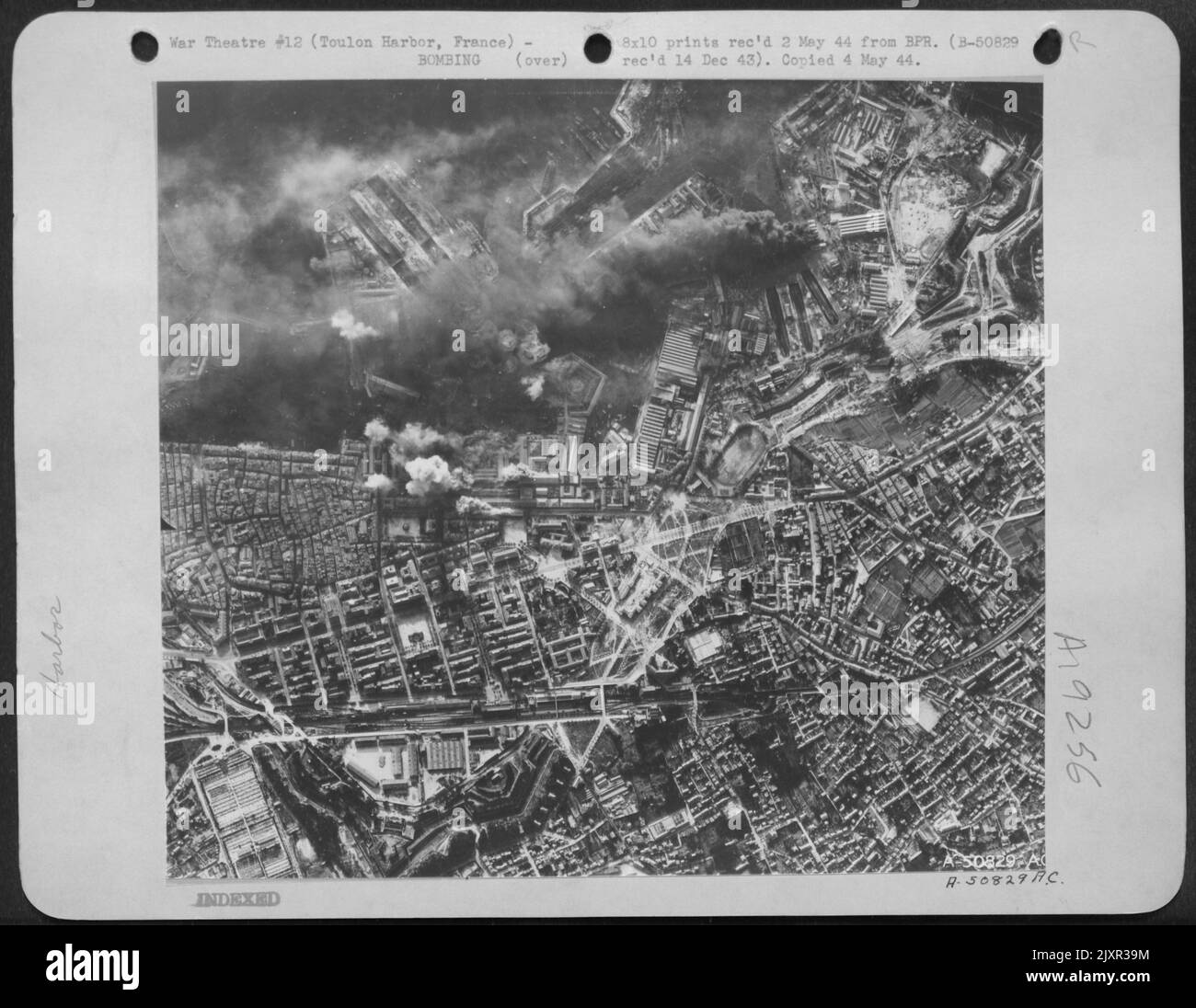 La zone du Nouveau bassin du port de Toulon prend un battement des forteresses de vol USAAF. Dans cette région se trouvent des quais secs, des magasins, un dépôt de charbon et un arsenal. La fumée noire à l'extrême gauche provient des ateliers de réparation, tandis que la grande bouffée blanche au centre droit se trouve dans le Banque D'Images