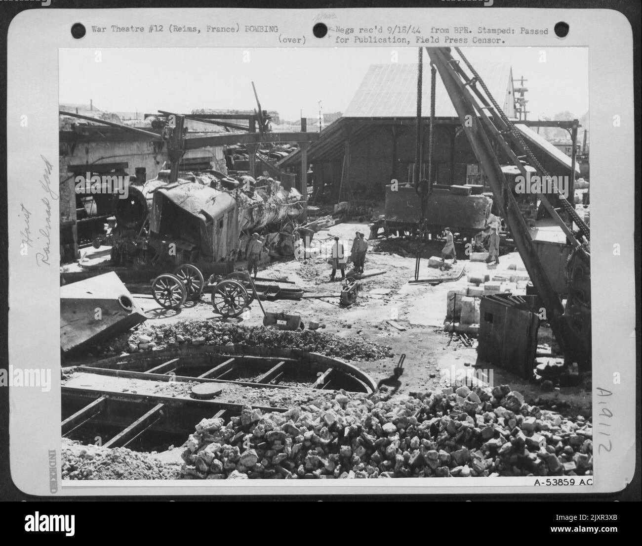 Derrière une pile de gravats et à travers une plaque tournante en crasse, les officiers alliés inspectent deux locomotives déchirées et déchirées à l'écart des coups par des bombes larguées sur des bombardiers lourds de 8th AF. Des rails tordus, des camions déchirés et des gravats embrayent la scène. Le travail est Banque D'Images