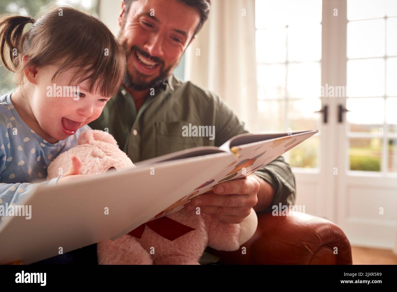 Père avec le syndrome de Down fille lisant le livre à la maison ensemble Banque D'Images