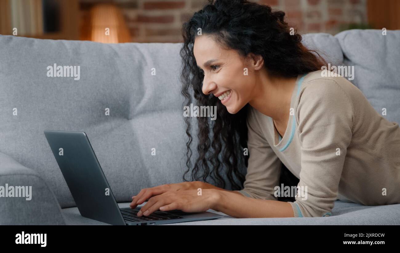 Vue latérale une femme heureuse couchée sur un canapé à la maison salon dactylographie clavier d'ordinateur portable travail en ligne commande livraison à partir de l'ordinateur de la boutique en ligne Banque D'Images