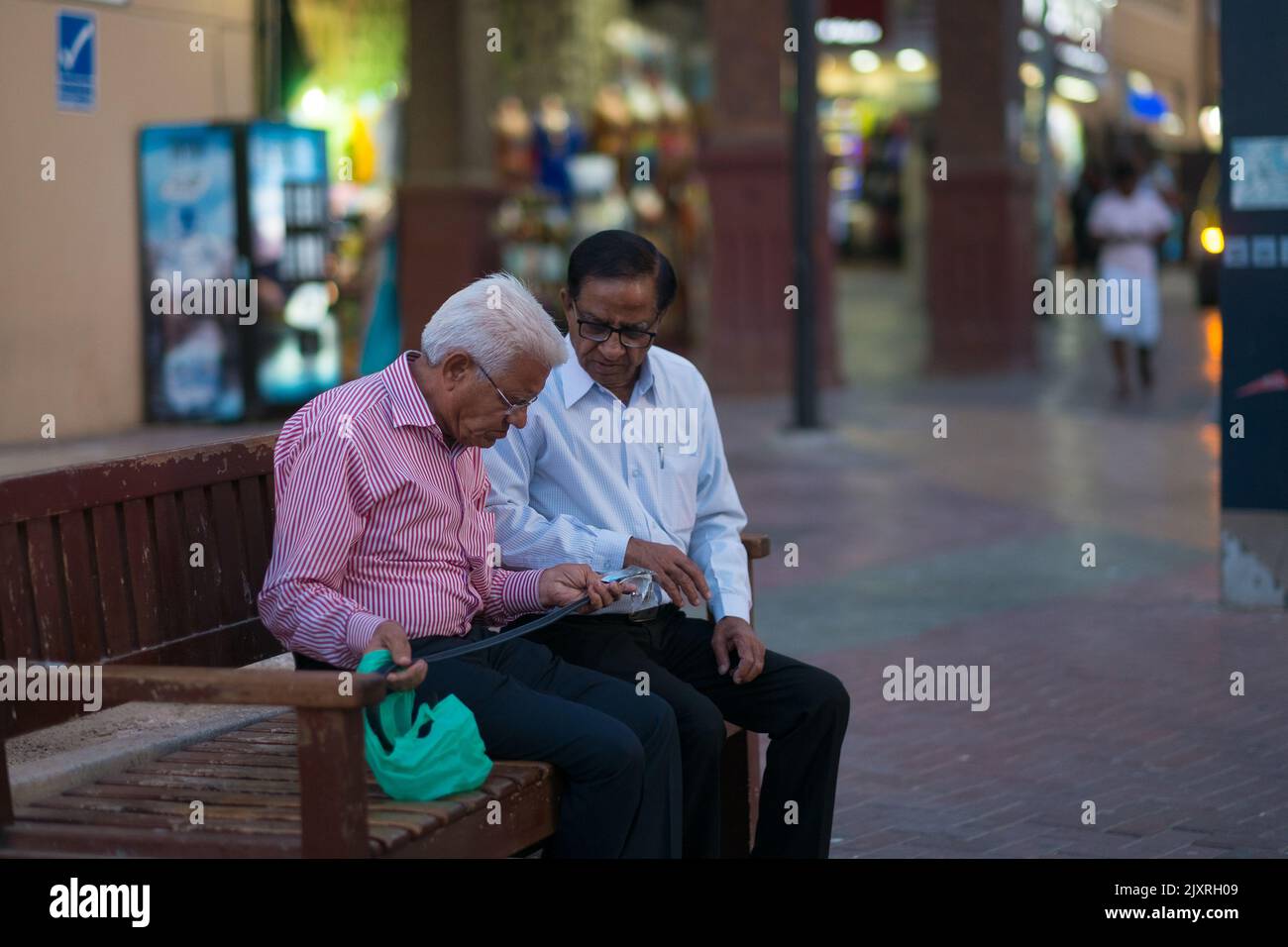 Deux vieux hommes portant des lunettes, des chemises à boutons et des pantalons sont assis sur un banc pour inspecter une ceinture qu'ils viennent d'acheter au souk textile (marché arabe). Banque D'Images