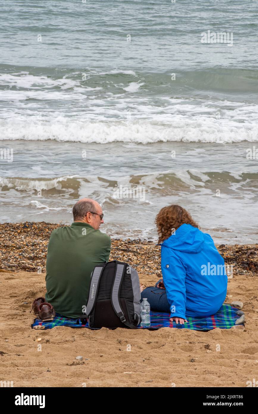 couple assis sur la plage ensemble, couple plus âgé discutant en étant assis sur la plage, couple en bord de mer, vagues s'écrasant sur la plage à swanage. Banque D'Images