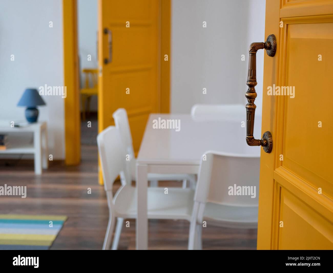 Chambre moderne avec portes jaunes, murs et mobilier blancs, mise au point sélective. Vue du salon par la porte entrouverte Banque D'Images