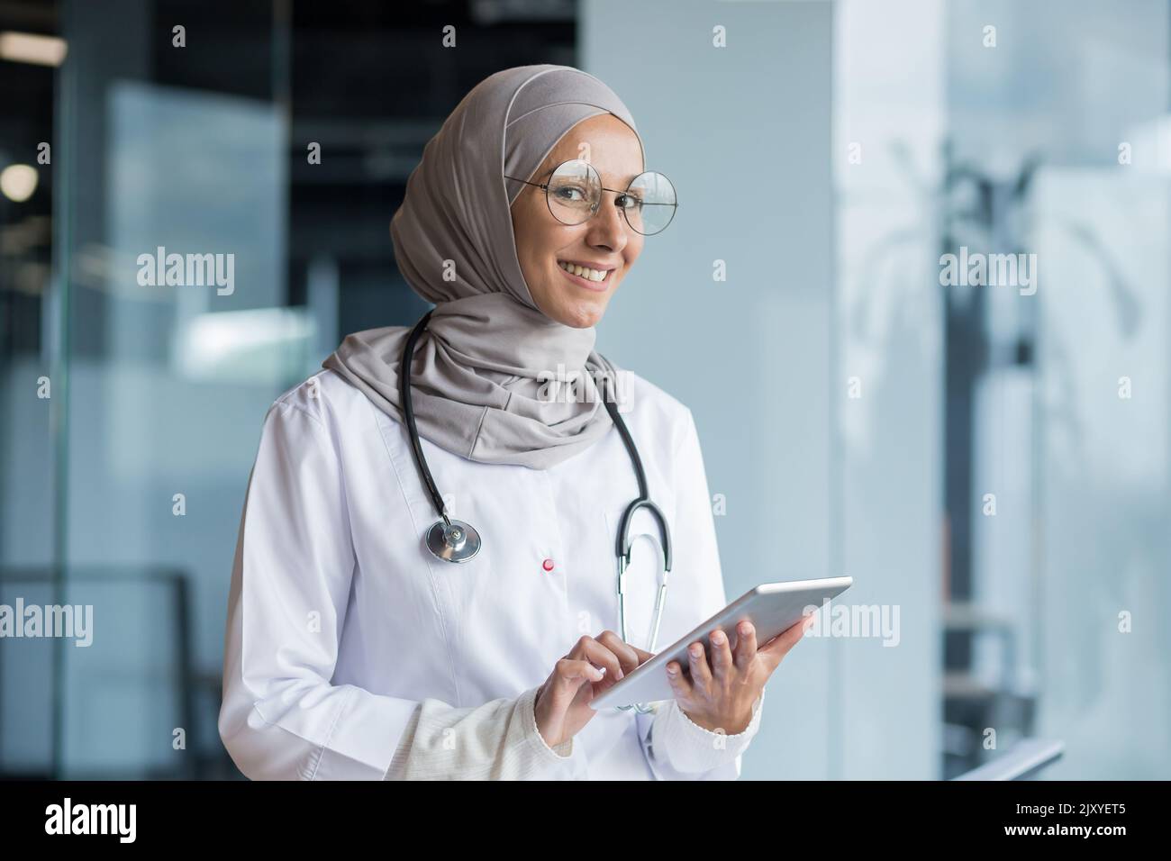 Portrait d'une femme musulmane médecin dans un hijab avec une tablette dans ses mains, le médecin travaille dans le bureau d'une clinique moderne, sourit et regarde la caméra. Banque D'Images