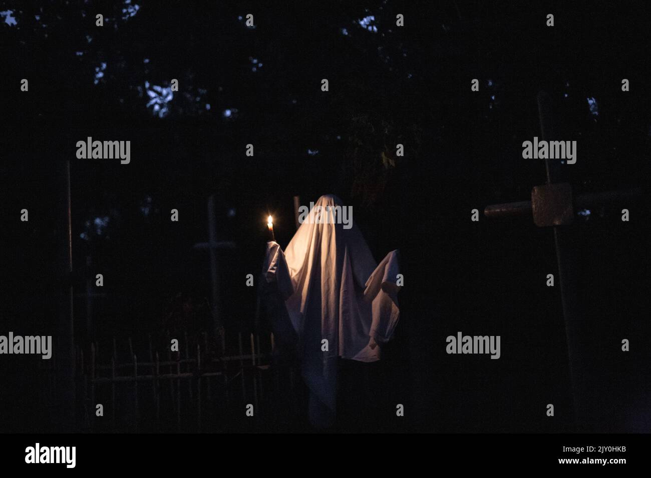 Fantôme tenant une bougie dans le cimetière entre les tombes pendant Halloween la nuit Banque D'Images