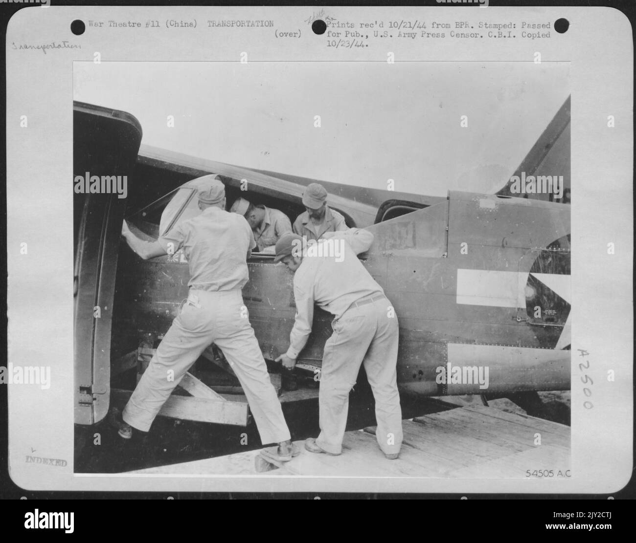 Un avion à l'intérieur d'un autre avion, ou de gros poissons mange peu de poisson, un fuselage de chasse P-40 Curtiss étant déchargé du gros ventre d'un navire de cargaison C-47 de Douglas dans une base aérienne américaine en avant en Chine. Banque D'Images