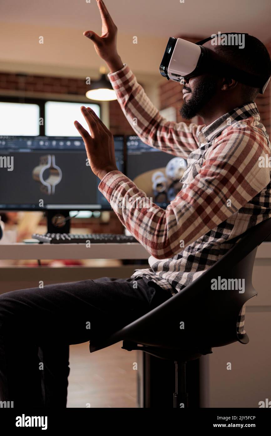 Un ingénieur afro-américain fabrique des engins mécaniques à l'aide de lunettes vr avec un logiciel de simulation et de CAO 3D sur ordinateur. Techinican développe des machines industrielles avec des lunettes interactives. Banque D'Images
