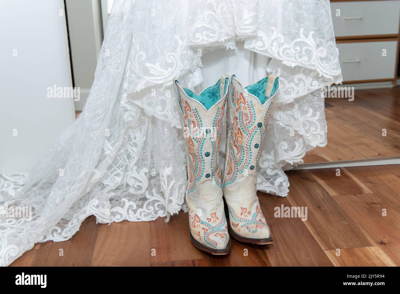 Robe de dentelle blanche de la mariée est associée à des bottes de cowgirl blanches brodées pour une cérémonie de mariage de l'Ouest. Banque D'Images