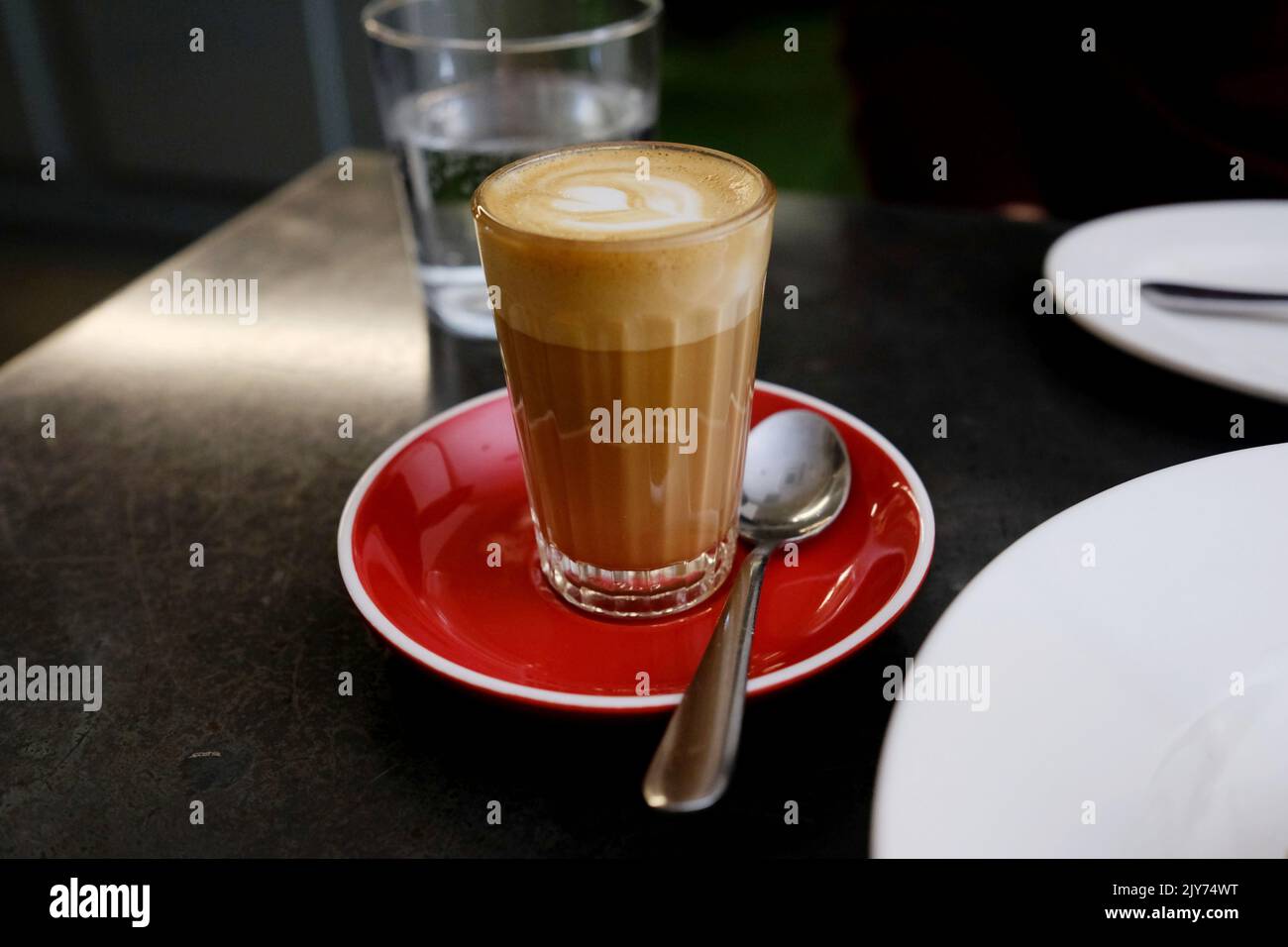 Un café piccolo dans un verre sur une soucoupe rouge au Bella Brutta, un restaurant australien italien moderne à Newtown, Sydney — Nouvelle-Galles du Sud, Australie Banque D'Images