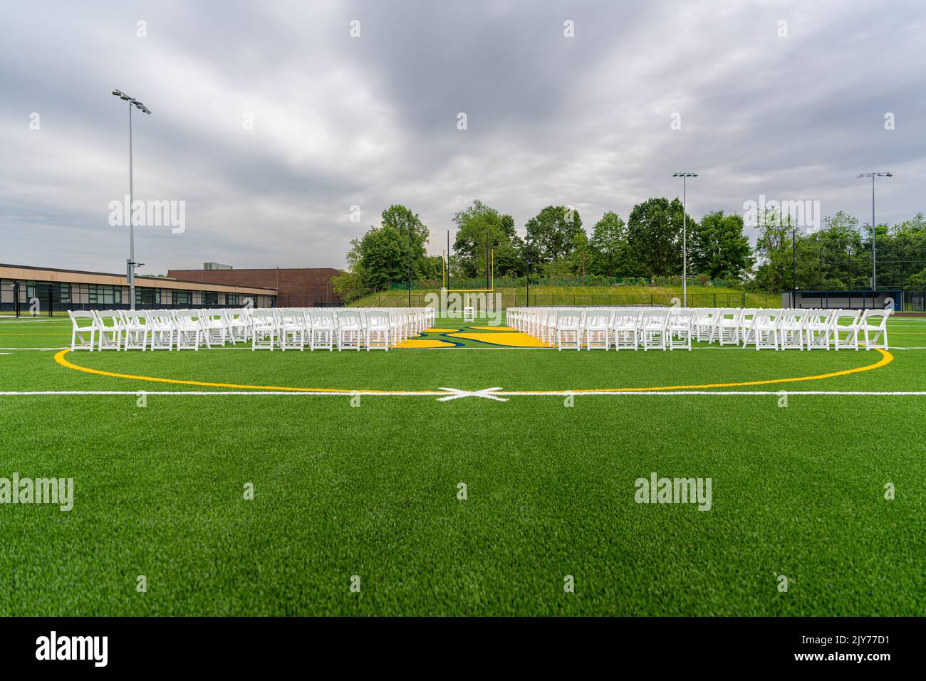 Chaises blanches disposées en rangées sur un terrain d'athlétisme en gazon synthétique vert pour une cérémonie de remise des diplômes du lycée. Banque D'Images