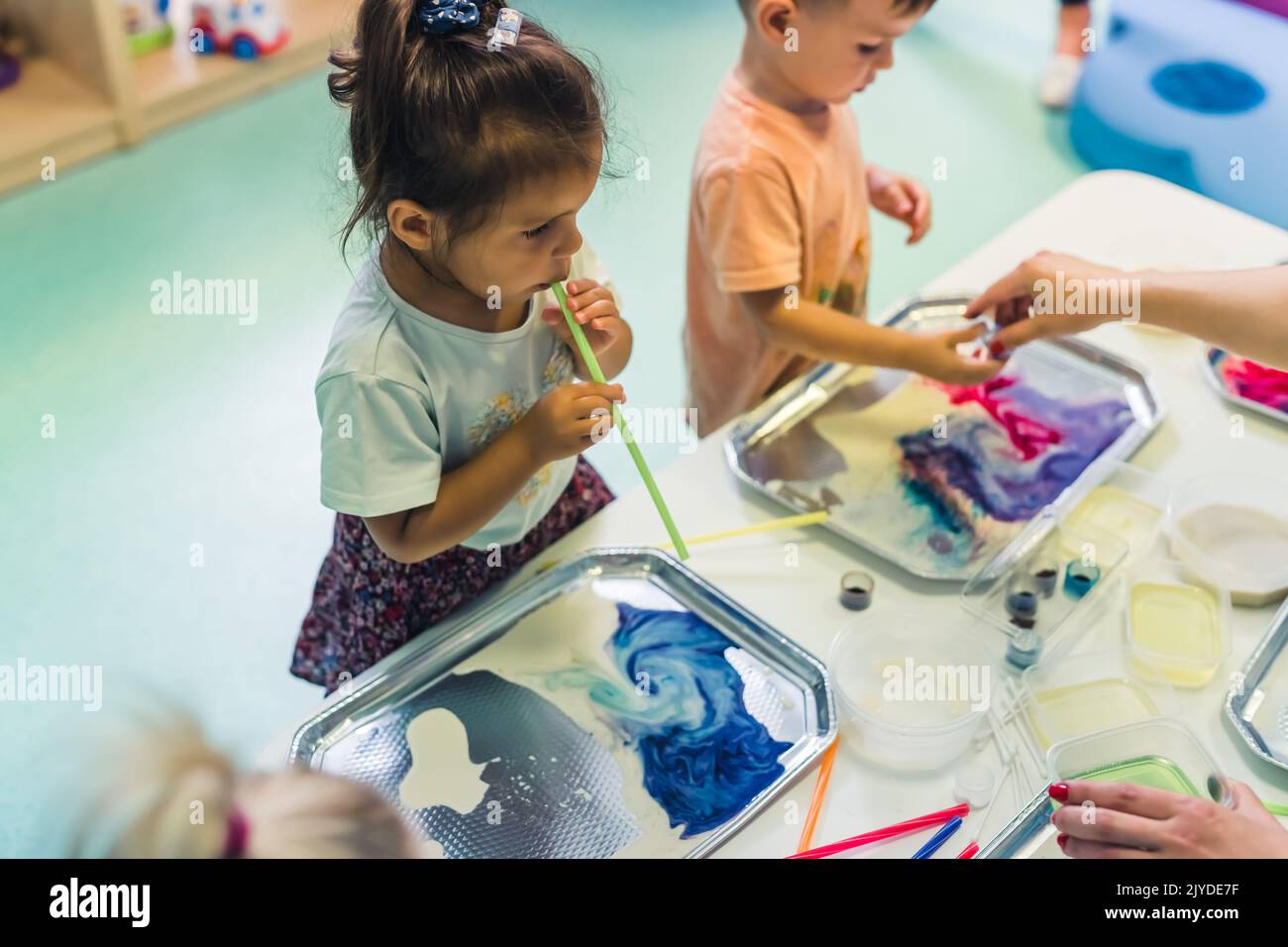 École maternelle multiculturelle. Les tout-petits jouant avec des pailles rayées et la peinture au lait, en utilisant des colorants alimentaires non toxiques pour les couleurs. Activité créative des enfants pour utiliser leurs sens et le développement du cerveau. Peinture au doigt. Photo de haute qualité Banque D'Images