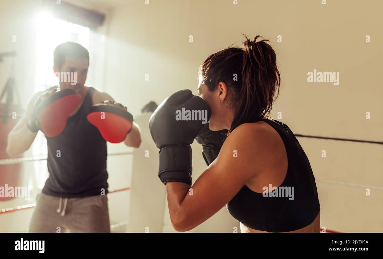 Boxeur féminin ayant une session d'entraînement avec son entraîneur dans un anneau de boxe. Une jeune femme sportive qui fait des étincelles avec son entraîneur personnel à la salle de gym. Banque D'Images