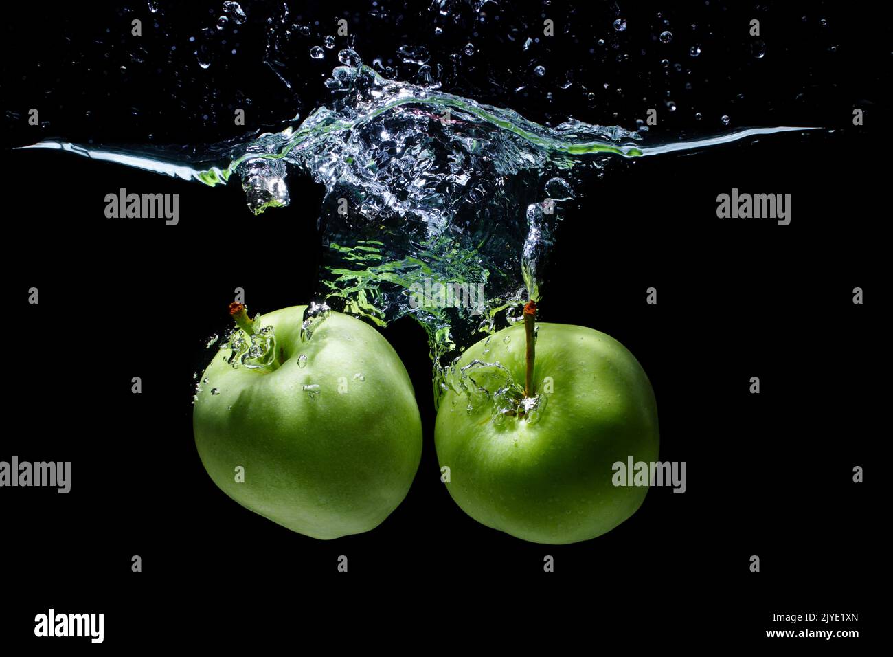 Deux pommes vertes tombèrent dans l'eau avec des éclaboussures isolées sur fond noir Banque D'Images