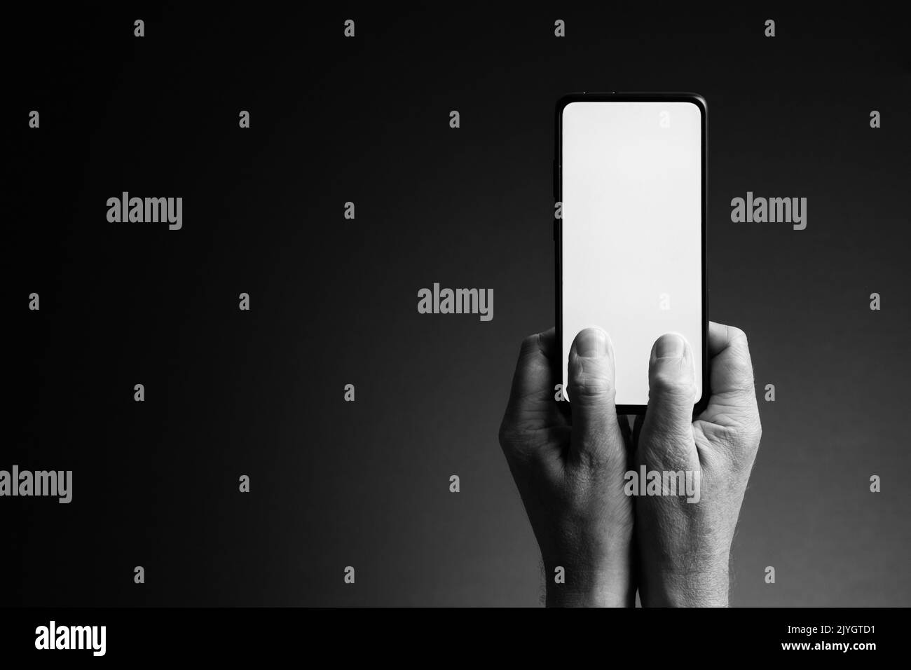 Image en noir et blanc des mains de l'homme tenant le smartphone et l'envoi de SMS avec écran blanc vierge isolé sur fond sombre avec espace de copie Banque D'Images