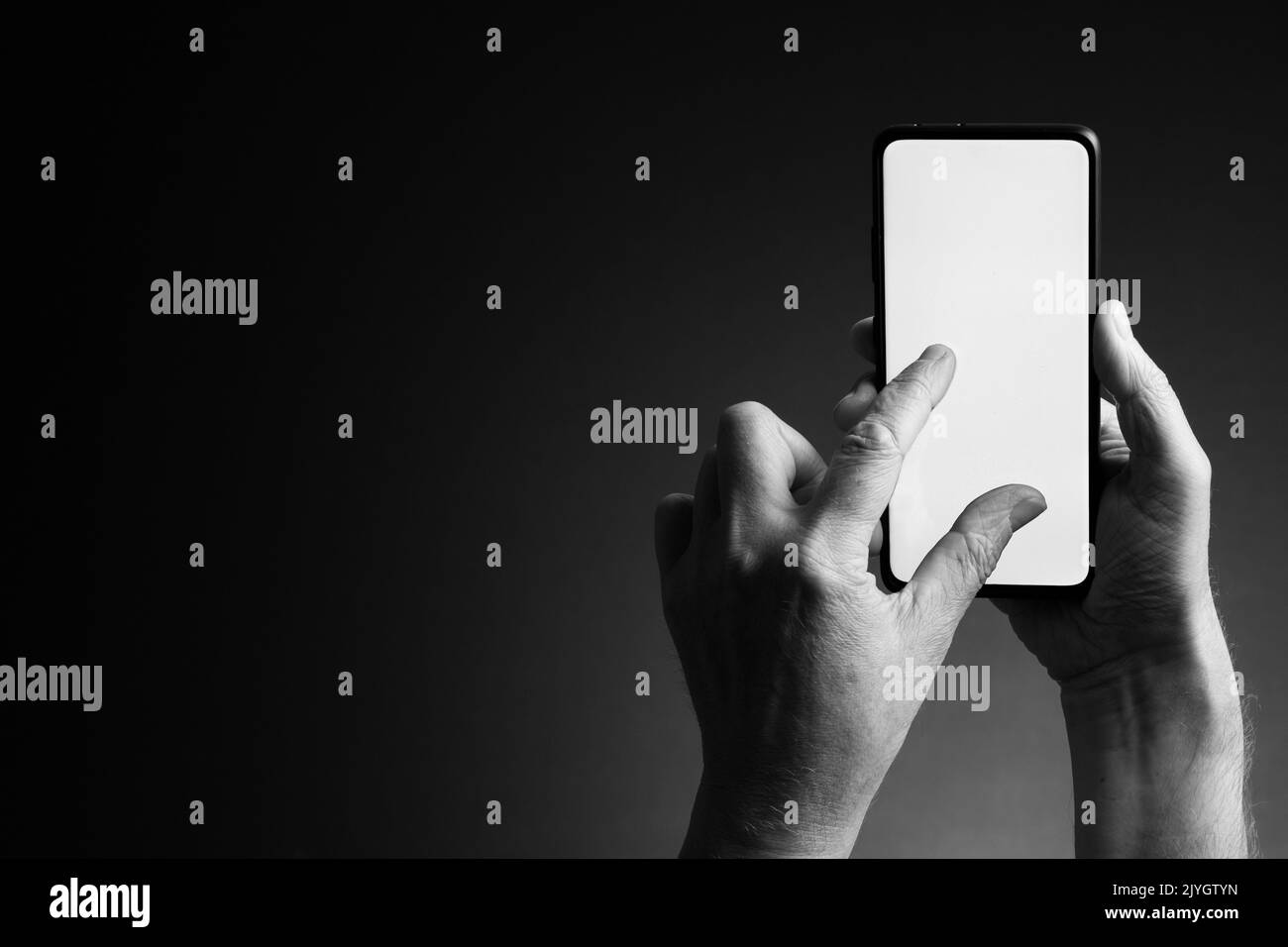 Image en noir et blanc des mains de l'homme tenant le smartphone et zoom par pincement avec écran blanc vierge isolé sur fond sombre avec espace de copie Banque D'Images