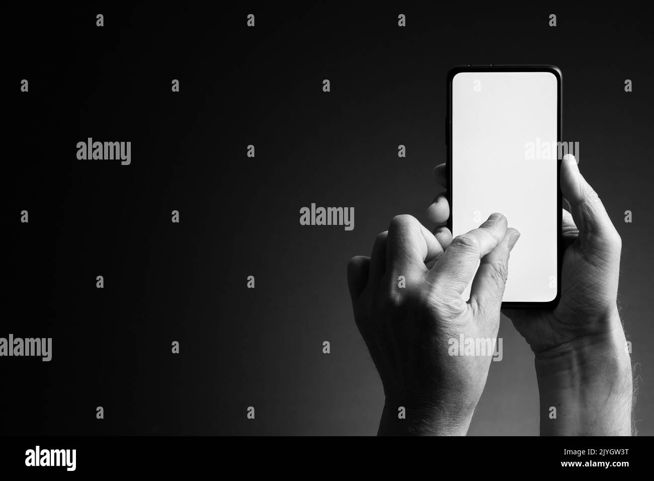 Image en noir et blanc des mains de l'homme tenant le smartphone et zoom par pincement avec écran blanc vierge isolé sur fond sombre avec espace de copie Banque D'Images