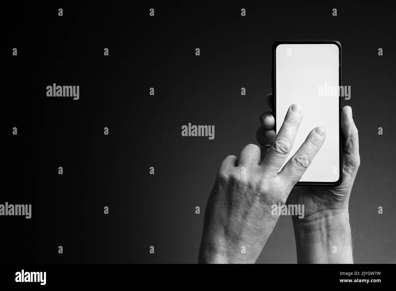 Image en noir et blanc des mains de l'homme tenant le smartphone et panoramique à deux doigts avec écran blanc vierge isolé sur fond sombre avec espace de copie Banque D'Images
