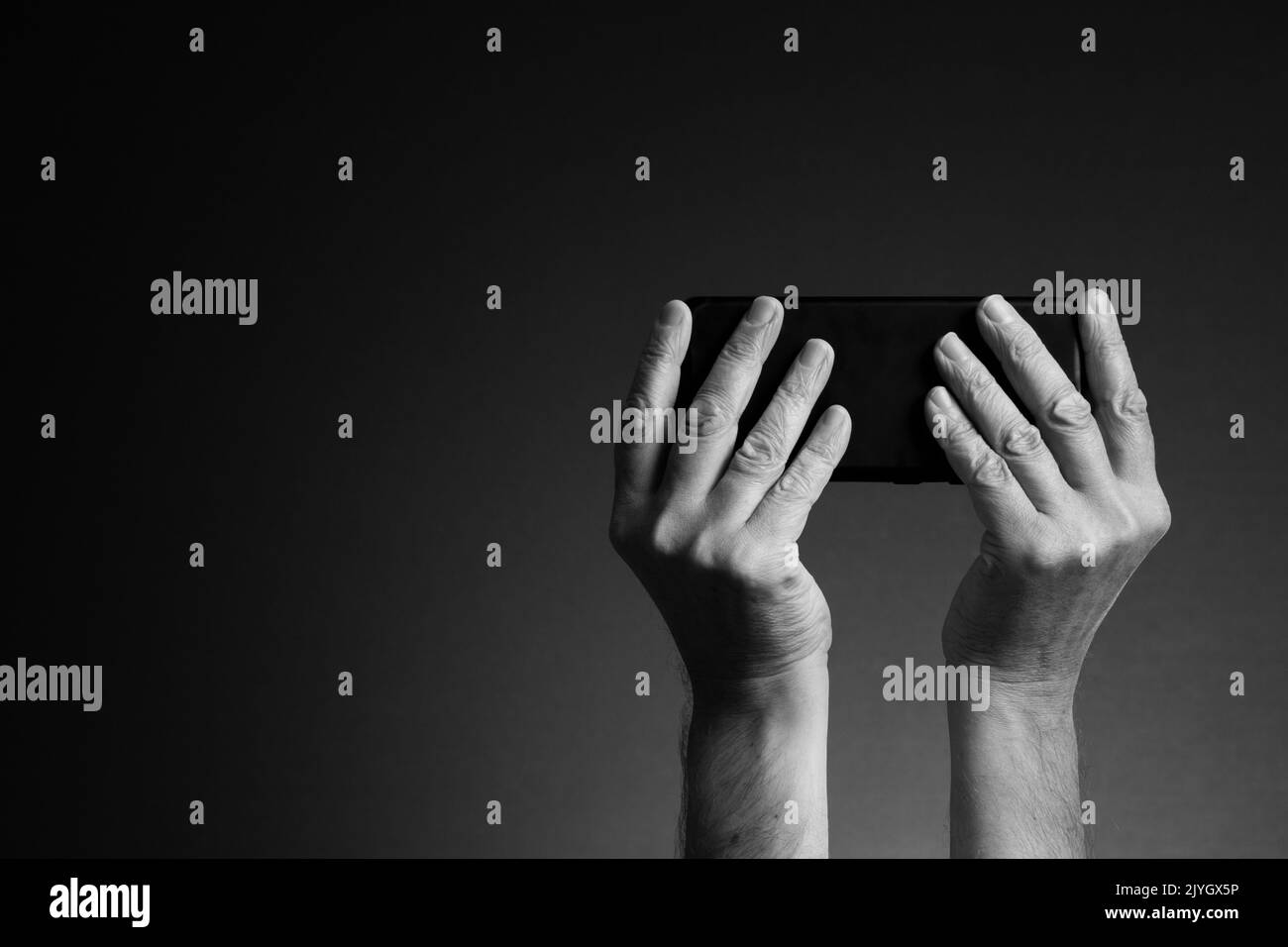 Image en noir et blanc, vue arrière des mains de l'homme tenant le smartphone horizontalement et l'envoi de SMS ou de jeux isolés sur un arrière-plan sombre avec espace de copie Banque D'Images