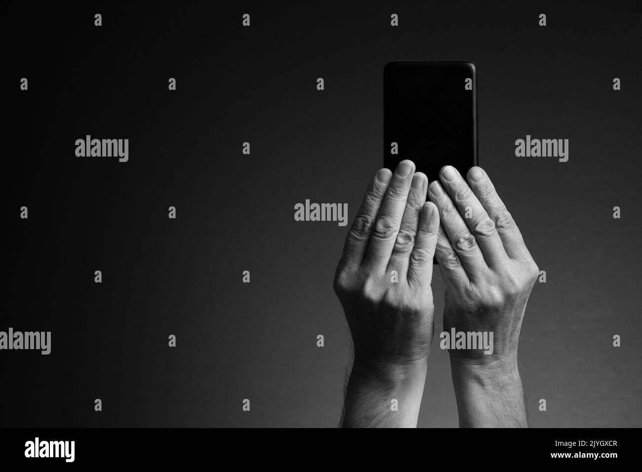 Image en noir et blanc, vue arrière des mains de l'homme tenant le smartphone et texte isolé sur fond sombre avec espace de copie Banque D'Images