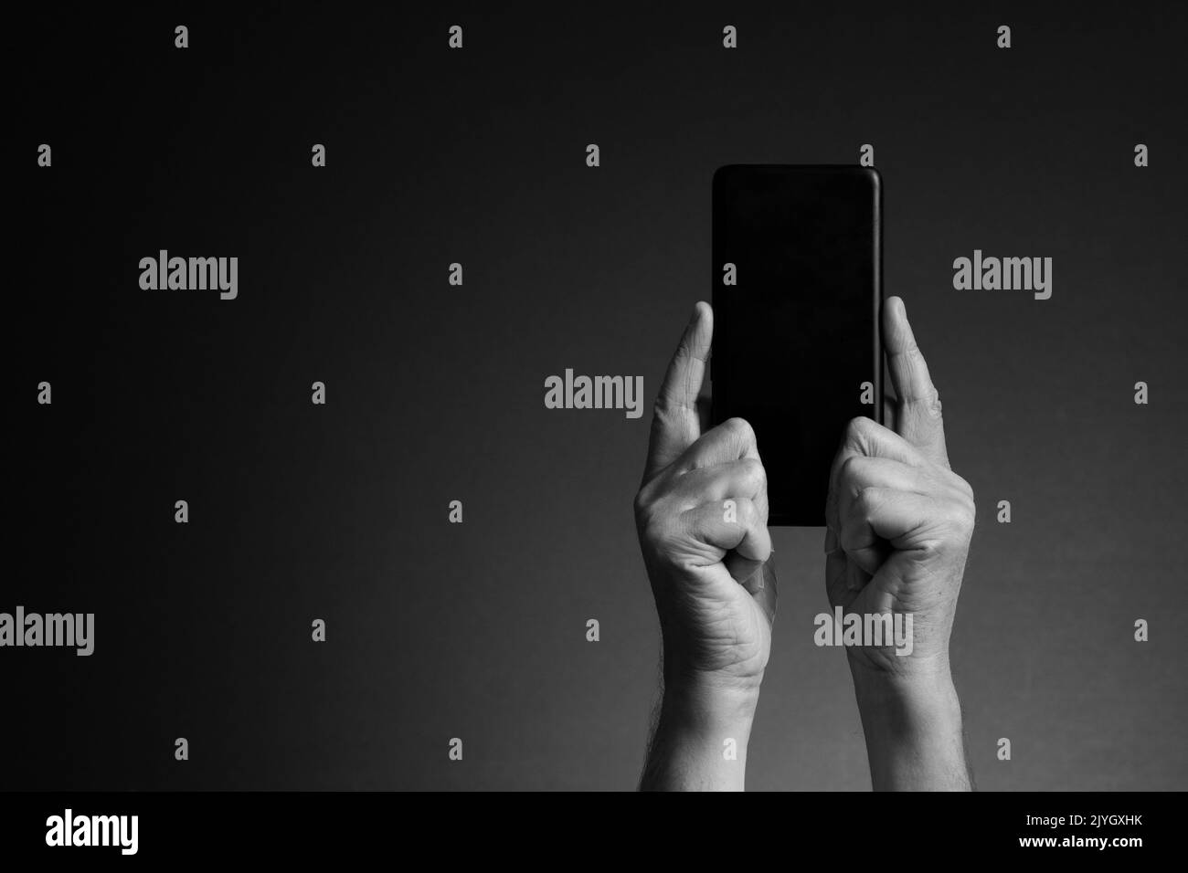 Image en noir et blanc, vue arrière des mains de l'homme tenant le smartphone et texte isolé sur fond sombre avec espace de copie Banque D'Images