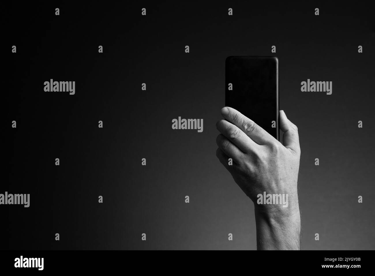 Image en noir et blanc, vue arrière de la main de l'homme tenant le smartphone isolée sur fond sombre avec espace de copie Banque D'Images