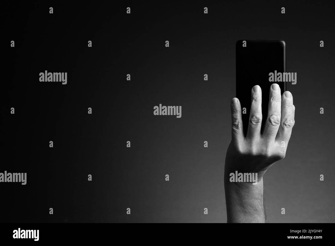 Image en noir et blanc, vue arrière de la main de l'homme tenant le smartphone isolée sur fond sombre avec espace de copie Banque D'Images