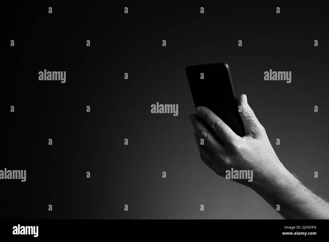 Image en noir et blanc, vue latérale de la main de l'homme tenant le smartphone isolée sur fond sombre avec espace de copie Banque D'Images