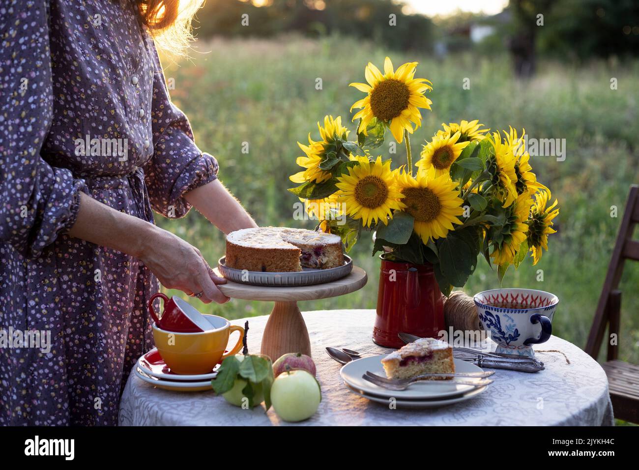 petite fille servant table à thé dans le jardin. tarte, vase avec tournesols et pommes sur une table Banque D'Images